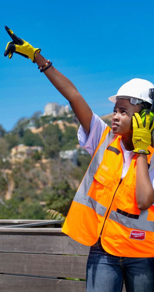 Operatrice al telefono in cantiere indica in alto.